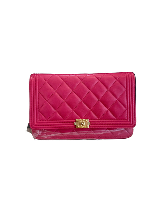 A bright pink quilted leather clutch wallet with a gold-tone interlocking CC clasp, displayed in front of a black Chanel box on a light beige surface.