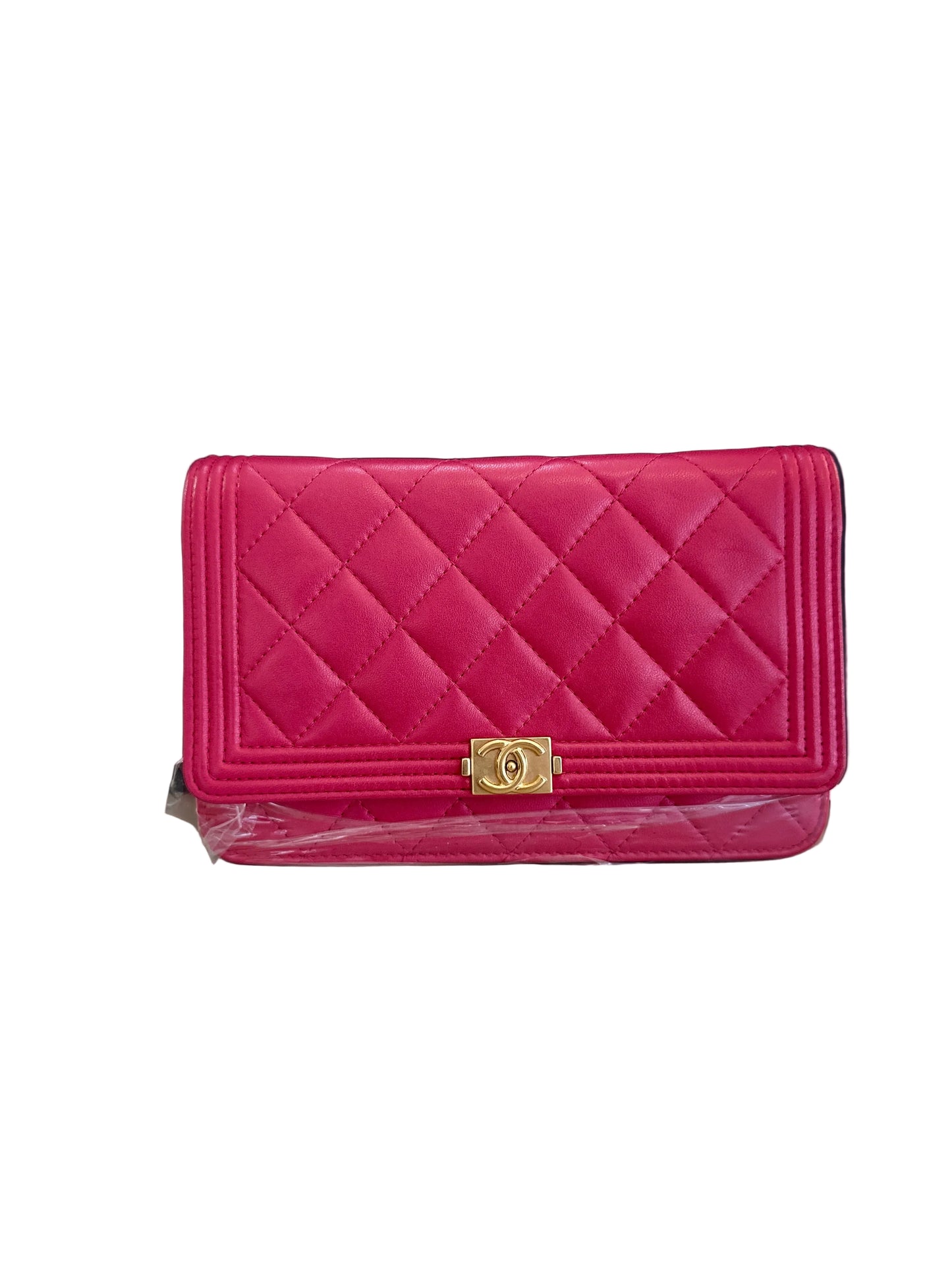 A bright pink quilted leather clutch wallet with a gold-tone interlocking CC clasp, displayed in front of a black Chanel box on a light beige surface.